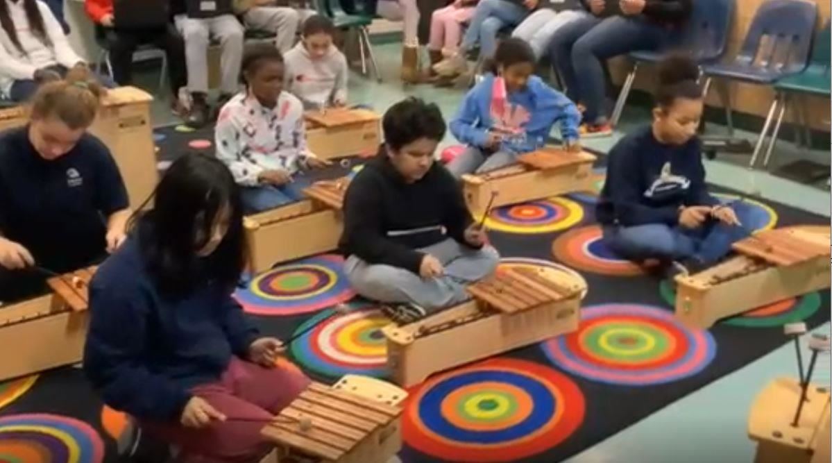 Group of students on a colorful carpet playing Martin Luther King Jr. song on xylophones.